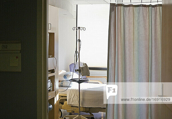 Krankenhauszimmer mit Bett und Sichtschutzvorhang.