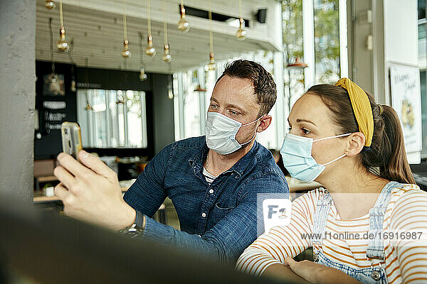 Two people wearing face masks  using a smart phone  waving during a face time call.