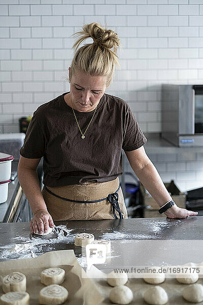 Blonde Frau mit brauner Schürze steht in einer Küche und backt dänisches Gebäck.
