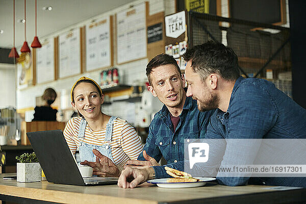 Two men and a woman meeting in a cafe  looking at a laptop