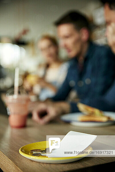 Menschen an einem Cafe-Tisch  eine Untertasse mit Kassenbon und Barzahlung