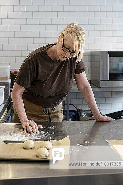 Woman in brown apron standing in a cafe kitchen  mixing baking danish pastry dough