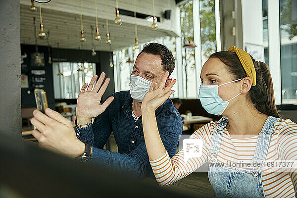 Zwei Personen mit Gesichtsmasken  die ein Smartphone benutzen  winken während eines Face-Time-Anrufs.