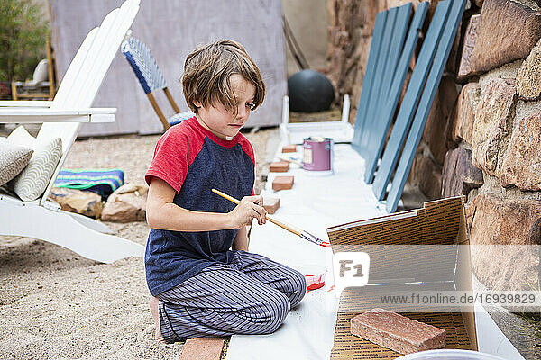 Seven year old boy using a paintbrush  painting cardboard
