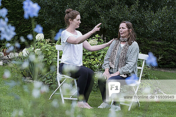 Frau und weibliche Therapeutin bei einer alternativen Therapiesitzung in einem Garten sitzend.