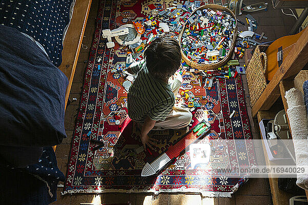 Junge sitzt zwischen Spielzeug auf seinem Schlafzimmerboden in einem Fleck Sonnenlicht