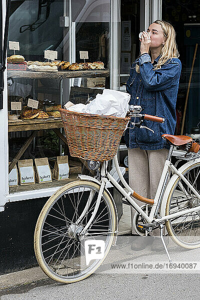 Junge blonde Frau steht neben einem Fahrrad vor einem abfallfreien Naturkostladen.