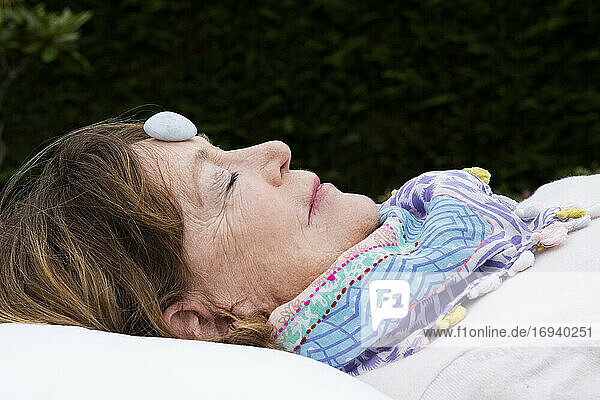Frau mit Stein auf der Stirn während einer alternativen Therapiesitzung in einem Garten.