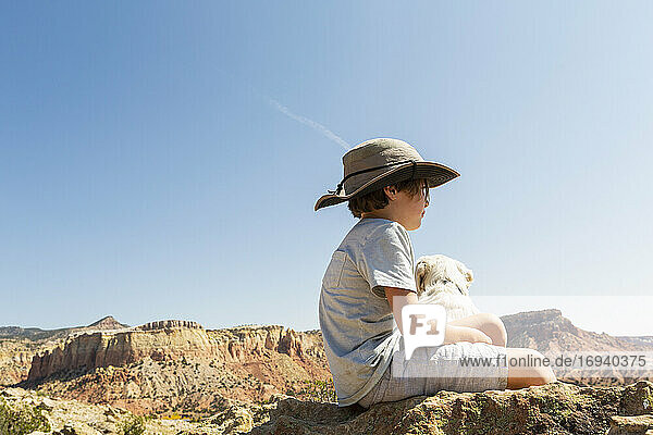 Junge sitzt mit seinem Hund auf einem Felsen