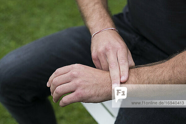 Ein Mann sitzend  zwei Finger am gegenüberliegenden Handgelenk  EFT-Berührungstherapie