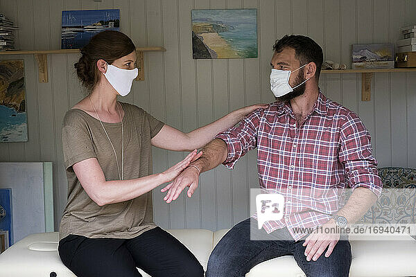 Therapeut und Klient mit Gesichtsmasken  Berührung mit ausgestrecktem Arm