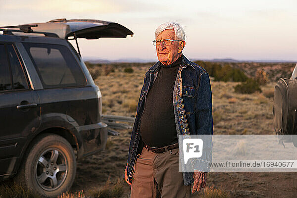 Älterer Mann steht zwischen SUV-Autos bei Sonnenuntergang  Galisteo Basin