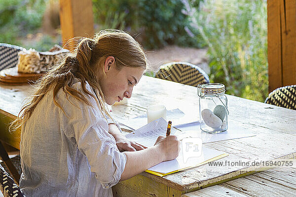 Teenager-Mädchen schreibt draußen auf der Terrasse bei Sonnenuntergang.