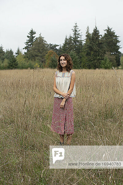 Porträt eines glücklichen siebzehnjährigen Mädchens  das in einem Feld mit hohen Gräsern steht