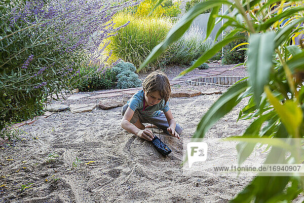 7 Jahre alter Junge spielt im sandigen Garten mit seinem Spielzeugschiff.