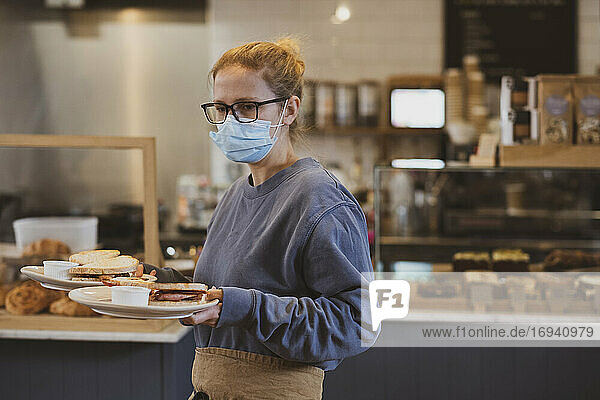 Waitress wearing face mask working in a cafe  carrying plates of food.