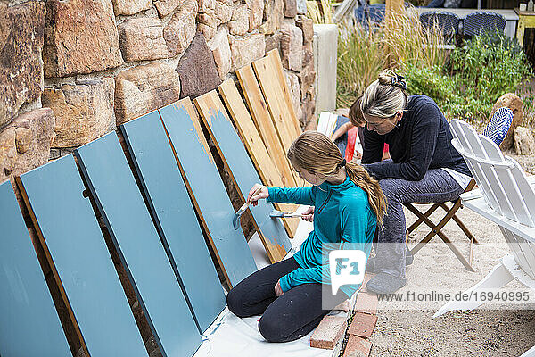 Teenager-Mädchen und ihre Mutter malen Holzregale blau auf einer Terrasse