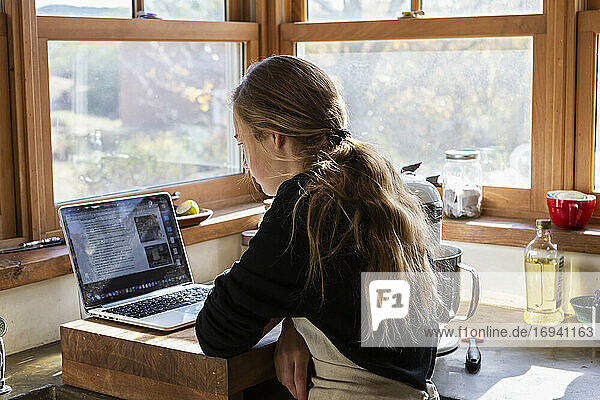 Teenager-Mädchen in einer Küche nach einem Backrezept auf einem Laptop.