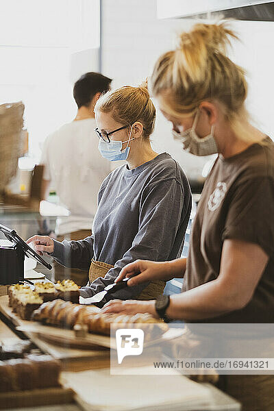 Kellnerin mit Gesichtsmaske  die in einem Café arbeitet und Essen zubereitet.