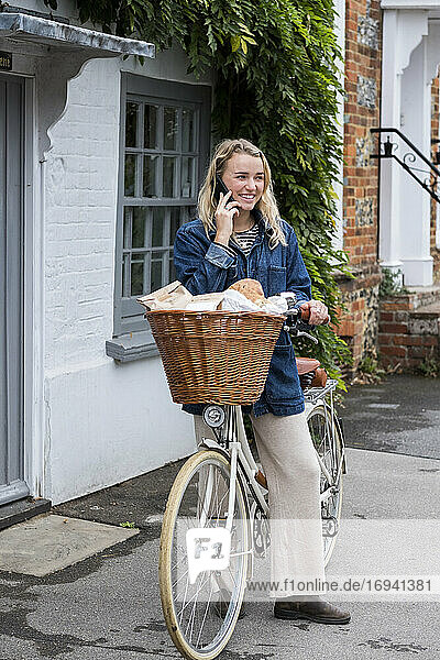 Young blond woman on bicycle with basket  talking on mobile phone.