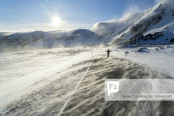 Mann jubelt auf eisiger leerer Straße entlang der Barentssee während des arktischen Sturms  Berlevag  Varanger Halbinsel  Finnmark  Norwegen  Skandinavien  Europa
