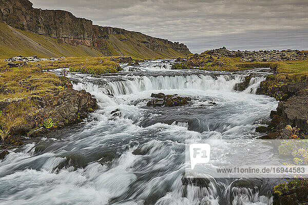 Eine klassische isländische Landschaft  ein Fluss  der am Fuße einer Klippe entlangfließt  Der Fluss Fossalar  in der Nähe von Kirkjubaejarklaustur  Island  Polarregionen