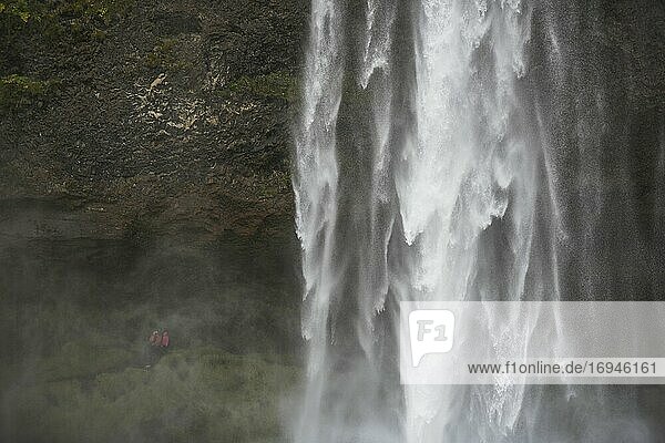 Touristen spazieren hinter dem Seljalandsfoss  einem berühmten Wasserfall an der Route 1 in Südisland (Sudurland)