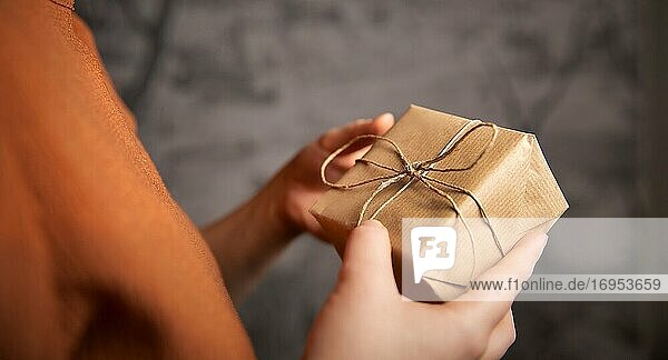 Junge Frau hält eine Kraft-Geschenk-Box  in einfachen braunen Papier eingewickelt  Valentinstag  Geburtstag  Muttertag Geschenk oder Geschenk-Konzept selektiven Fokus  dunklen Hintergrund Nahaufnahme.
