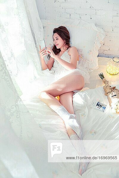 Eine schöne junge Frau liegt auf dem Bett und spielt mit ihrem Handy