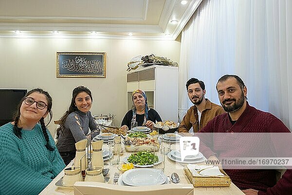 Eine muslimische türkische Familie isst zu Abend und alle schauen in die Kamera.