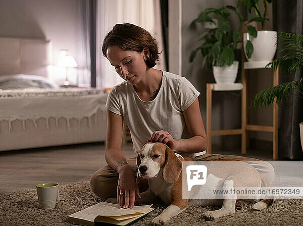 Frau mit Beagle liest Buch im Schlafzimmer