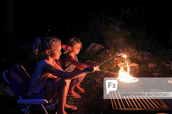 zwei Mädchen rösten Marshmallows über offenem Feuer  Camping im Sommer