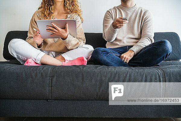 Crop-Paar auf dem Sofa mit Tablet und TV-Fernbedienung