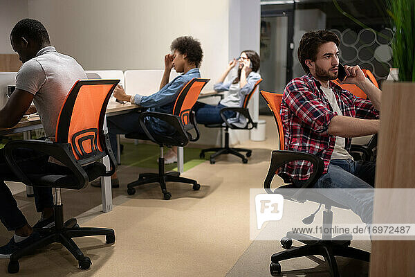Multiethnische Kollegen sitzen an Schreibtischen im Coworking Space