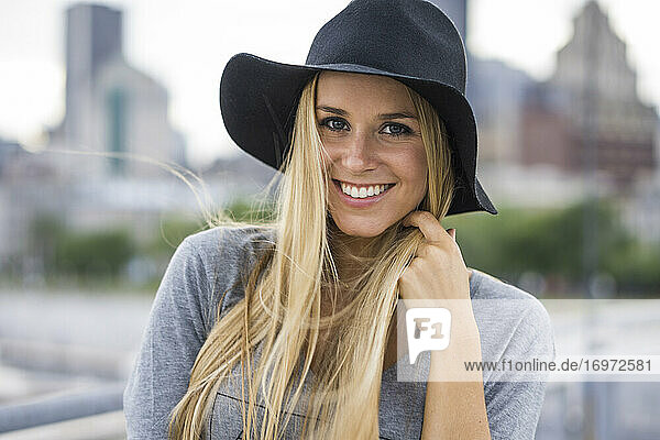 Blonde Frau lächelnd mit Hut und Stadtsilhouette hinter ihr