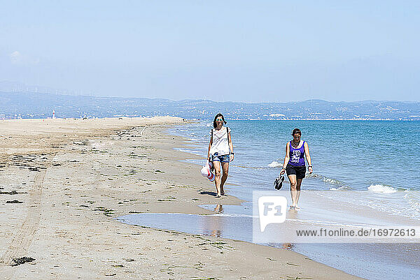 Front view of two women walking barefoot on seashore at beach