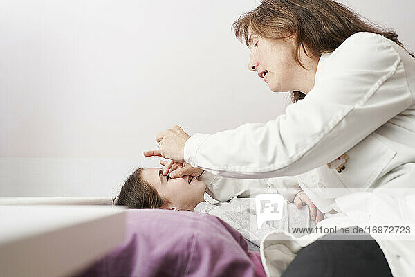 Eine Ärztin lächelt und gibt einem kleinen Mädchen in ihrem Bett Augentropfen. Hausarzt Konzept