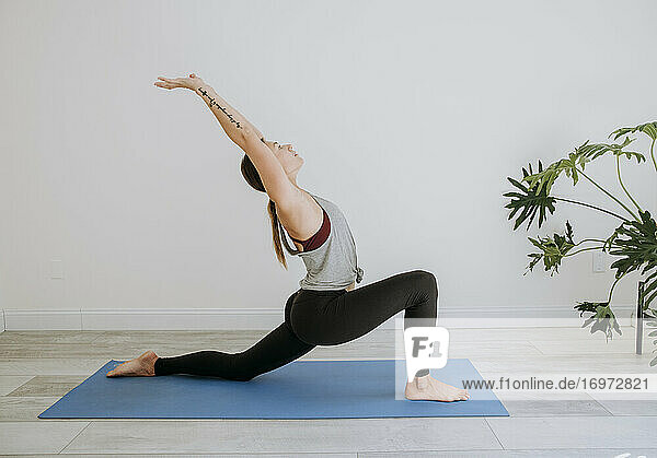 Woman practices yoga indoors on blue mat in simple white room