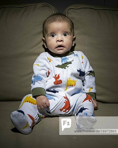 Ganzkörper-Neugeborenes im Pyjama  das in die Kamera schaut und auf dem Sofa sitzt