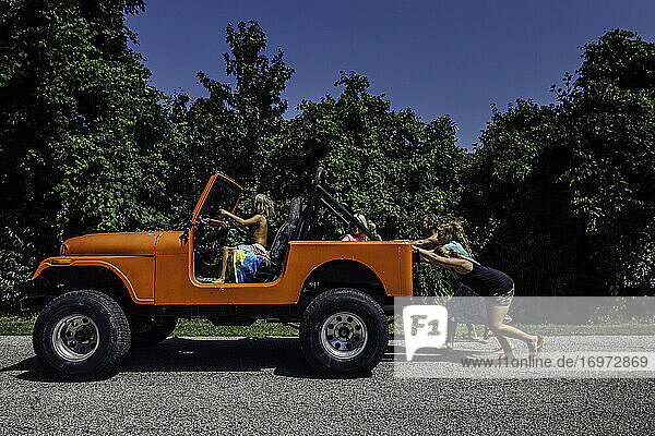Familie schiebt orangefarbenen Jeep  während Kleinkind lenkt