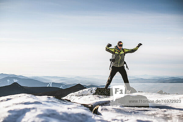 Mann mit Kamera springt von eisigem Felsen auf Berggipfel im Winter