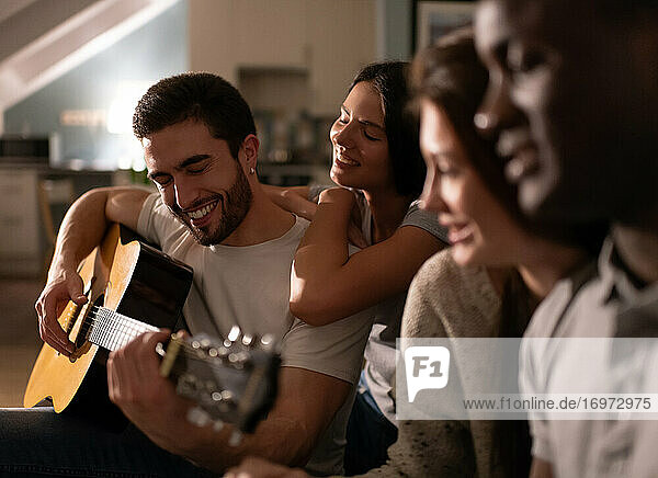 Fröhlicher Kerl spielt Gitarre bei einer Party mit Freunden