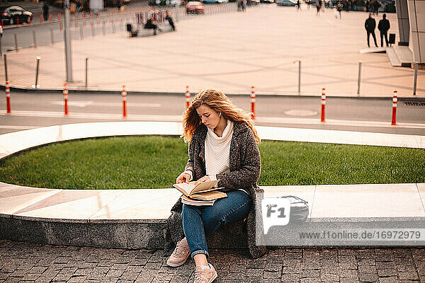 Teenager-Studentin  die im Herbst auf dem Campus sitzt und ein Buch liest