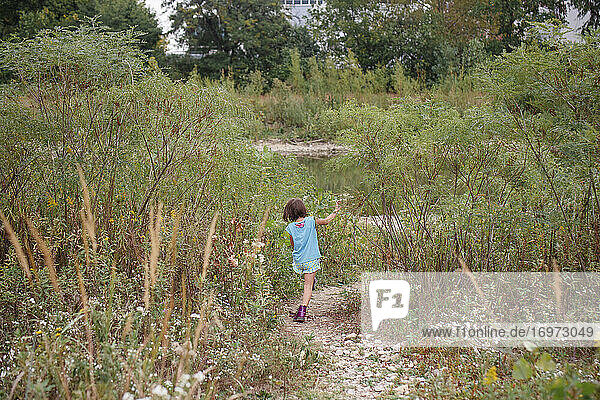 Ein kleines Mädchen geht durch hohes Gras und Wildblumen auf einem Steinweg