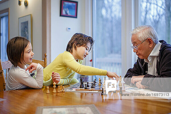 A boy and his sister sit at chessboard with grandfather making a move