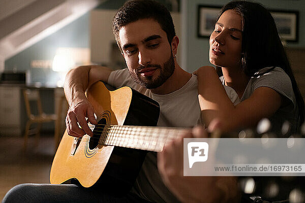 Junge Frau hört ihrem Freund beim Gitarrenspiel zu