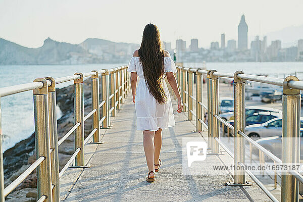 Rückenansicht einer jungen Frau in einem weißen Kleid  die auf einer Fußgängerbrücke geht