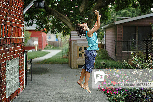 Ein kleiner Junge springt mit ausgestreckten Armen in die Luft in einem schönen Garten
