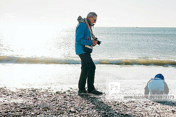 Opa fotografiert seinen Enkel an einem sonnigen Tag am Strand