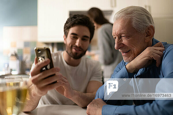 Älterer Mann betrachtet Fotos auf dem Smartphone seines Sohnes